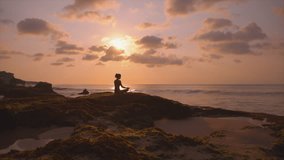 Silhouette of a slim woman on the beach at a beautiful sunset, Practice of yoga breathing techniques. Beautiful purple sunset on bali rocky beach. Female person in lotus position. Sport exercises - Powered by Shutterstock - Get 15% off with code: PIKWIZARD15