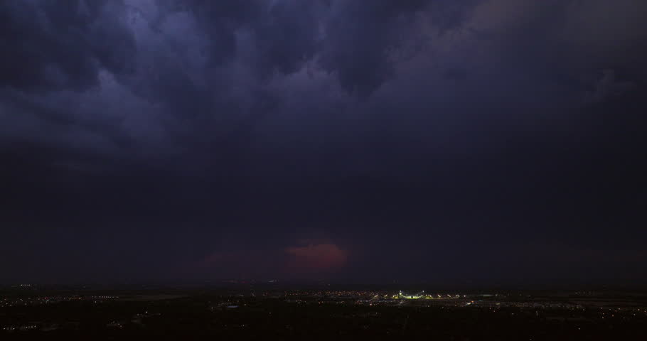 Cinematic aerial of dark storm clouds with lightning in the clouds in a dark sky with an ominous tone in this suburban establishing shot as a storm system moves in before causing hail and rain.