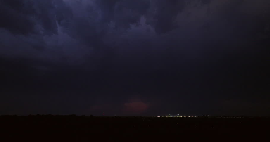 Cinematic aerial of dark storm clouds with dramatic lightning bolts striking after dusk in a dark sky with an ominous tone in this suburban establishing shot as the camera descends behind dark trees.