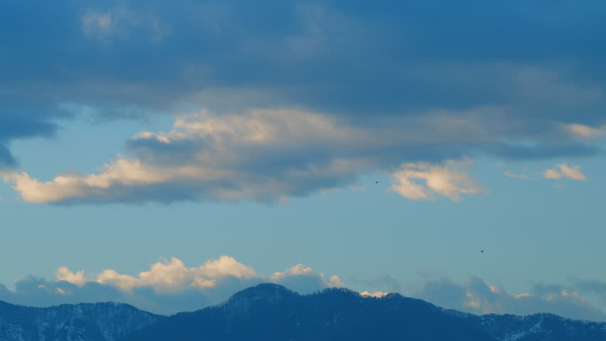 Bird Of Prey Fly In Sky. Eagle Flying Against Blue Sky With Clouds. Cloud Cover Over The Peaks Of The Mountains. Still.