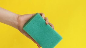 Vertical video. House chores. Domestic cleaning. Janitor services. Woman hands squeezing green pink washing sponges on isolated on yellow background copy space.