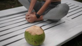 Close up of fresh green coconut ready to drink, mid adult story woman exercising outdoors, daytime.High quality 4k footage
