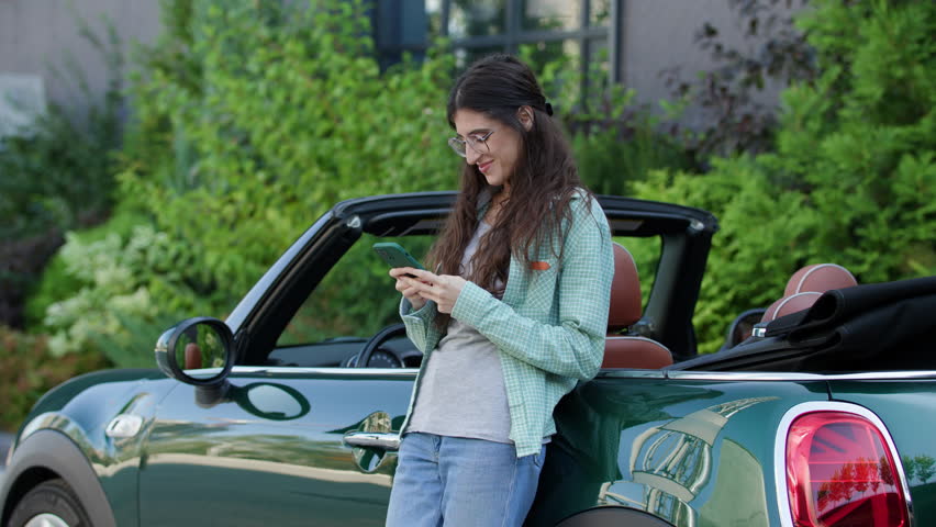 Female Browsing Smartphone Standing Outside by Convertible. Young adult driver surfing web using cellphone near the car. | Shutterstock HD Video #1109067215