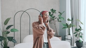 Young happy ethnic African American woman in headphones dances and gets high from good music gets positive emotions listening to new album of popular pop artist stands in living room with white sofa - Powered by Shutterstock - Get 15% off with code: PIKWIZARD15