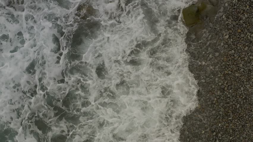 Ocean Waves Crash Over Rocky Boulders Along a Coastal Pebbled Beach with a Top View in Looc Bay, Philippines.