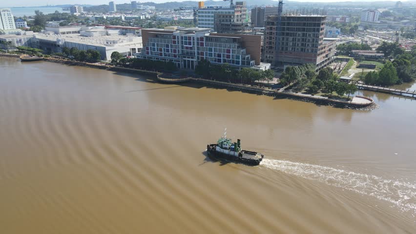 Sarawak, Malaysia – May 30, 2023: From above, a transportation boat gracefully sails along the winding path of the serene yellow river in Borneo, a tranquil journey through nature