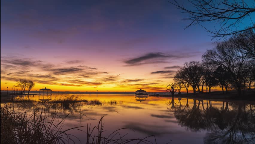 Fire red sunset sky lights up clouds and reflection on placid lake, golden hour time lapse