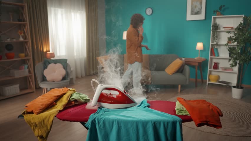 A man is passionately talking on his cell phone and walking around the room. At this time, an iron that has been turned on begins to smoke. The man does not notice what is happening. Slow motion