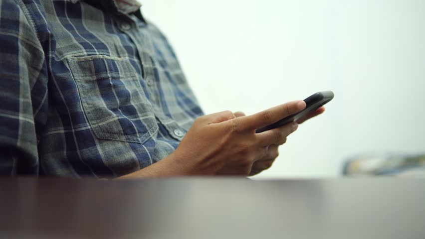 Male hands typing on smartphone, wearing a shirt, while sitting, behind the table, side view | Shutterstock HD Video #1109080277