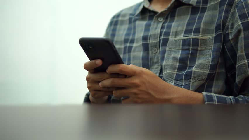 Male hands typing on smartphone, wearing a shirt, while sitting, behind the table, side view | Shutterstock HD Video #1109080279