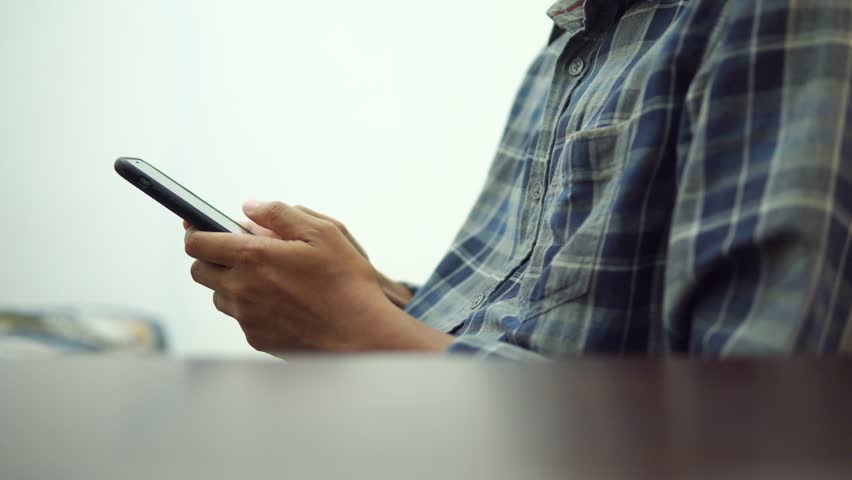Male hands typing on smartphone, wearing a shirt, while sitting, behind the table, side view | Shutterstock HD Video #1109080281
