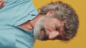 Vertical video, Close-up of an elderly grey-haired bearded man wearing a blue shirt looking camera wink eye blink isolated on orange background in studio