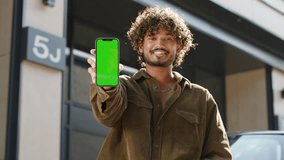 20s Man Showing Smartphone Green Screen at Camera. Indian man holding chroma key cellphone screen standing outside. - Powered by Shutterstock - Get 15% off with code: PIKWIZARD15