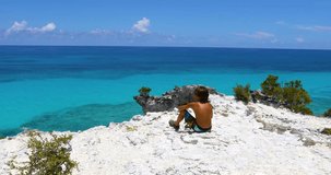 Static video of a young boy looking out from a cliff into the ocean in Exuma in the Bahamas.