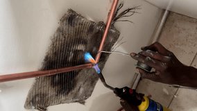 Vertical shot of hands of black plumber soldering elbow connection of new copper pipe using a blow torch inside of house. - Powered by Shutterstock - Get 15% off with code: PIKWIZARD15