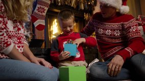 Excited cute kid unwrapping gift box. Super happy little boy excited to get surprise present near decorated Christmas tree. Happy family sitting at fireplace. Cinematic Christmas eve RED camera - Powered by Shutterstock - Get 15% off with code: PIKWIZARD15