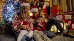Happy family gathered together on Christmas eve near xmas tree. Young beautiful parents in red Santa hats and little baby daughter, preschooler son enjoying time together at cozy fireplace RED 4K - Powered by Shutterstock - Get 15% off with code: PIKWIZARD15
