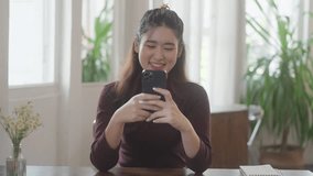 Happy asian girl using mobile smart phone watching online social media with funny content
