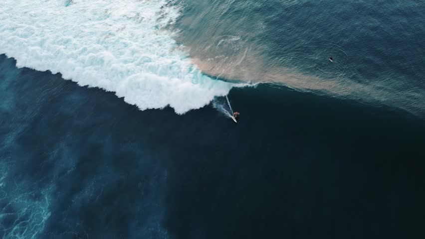 Top down video of a surfer catching a wave in sunset, bending and rolling on it, doing tricks. A surfer runs his hand along the wave tube. Surfer lifestyle and extreme sports. Background surf video. Royalty-Free Stock Footage #1109101091