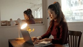 Young cheerful woman using headset for online talking sitting at the desk at home office. Pleasant female operator looking at the screen. Remote work concept.