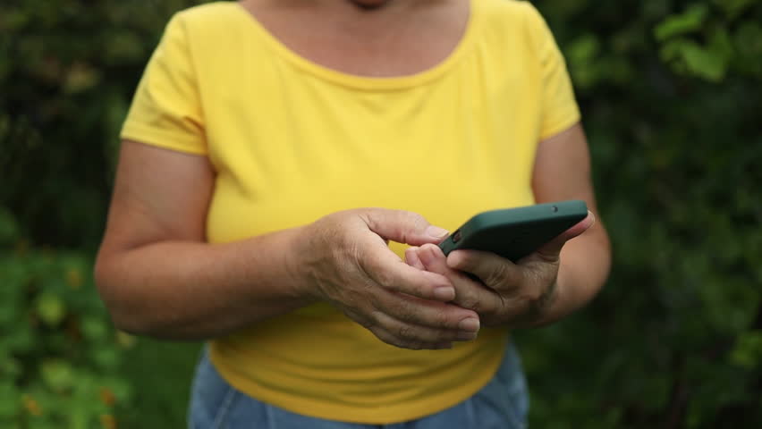 Portrait of middle aged attractive woman using her cellphone and text messaging while relaxing at summer garden | Shutterstock HD Video #1109101927
