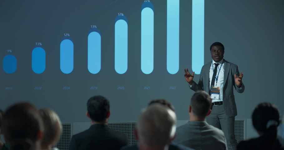 Corporate Event: Black Male Marketing Director Giving Presentation To Colleagues or Investors In Conference Room Of Innovative Startup Office. African Man Talking About Advertising Channels, Budget.