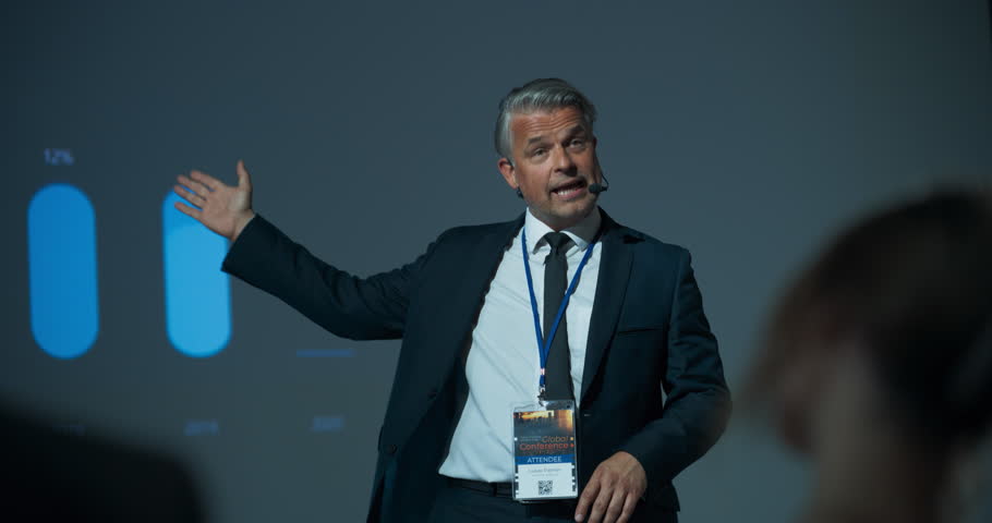 Successful Caucasian Businessman Giving Presentation At International Business Forum. Male Entrepreneur Pitching An Innovative Online Software Solution Startup To Diverse Audience Of Investors.