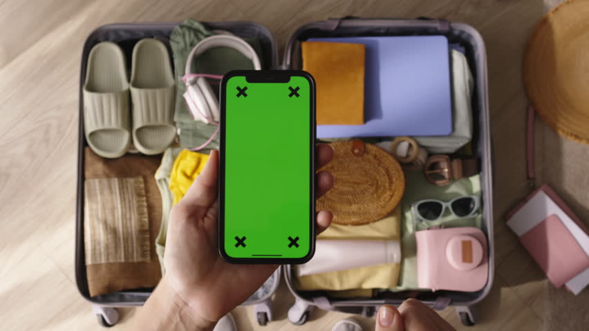 Chromakey phone packed suitcase. Female hands check presence of things necessary for trip in luggage note in list in smartphone. Attentive preparation for trip concept. Top view green screen mockup. Royalty-Free Stock Footage #1109117013
