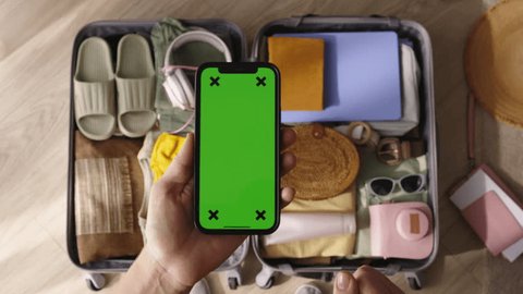 Chromakey phone packed suitcase. Female hands check presence of things necessary for trip in luggage note in list in smartphone. Attentive preparation for trip concept. Top view green screen mockup. Adlı Stok Video