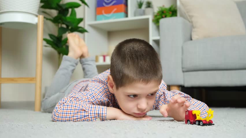 A little boy plays with a toy car lying on the floor alone.