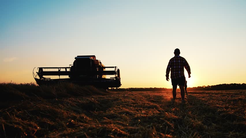 Teamwork concept. Silhouette two male farmers walking in a green field against sunset. Team farmers stand in a field on the background of agricultural machinery. Agronomists discuss harvest. Royalty-Free Stock Footage #1109123149
