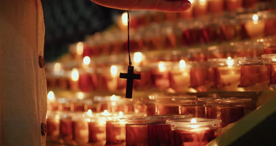 Woman praying in church. Adult girl clasping hands with cross near burning candles.