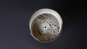 Pouring beer into glass from beer bottle, top view, close-up, black background. Slow Motion