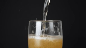 Pouring beer into glass from beer bottle, close-up, black background. Slow Motion