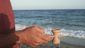 By the seaside, a man passionately plays Kendama, showcasing impressive tricks in this tranquil slow-motion video.