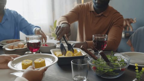 Cropped shot of African American father putting corn on cob on plate for daughter while taking care of kid during festive dinner at home Video de stock