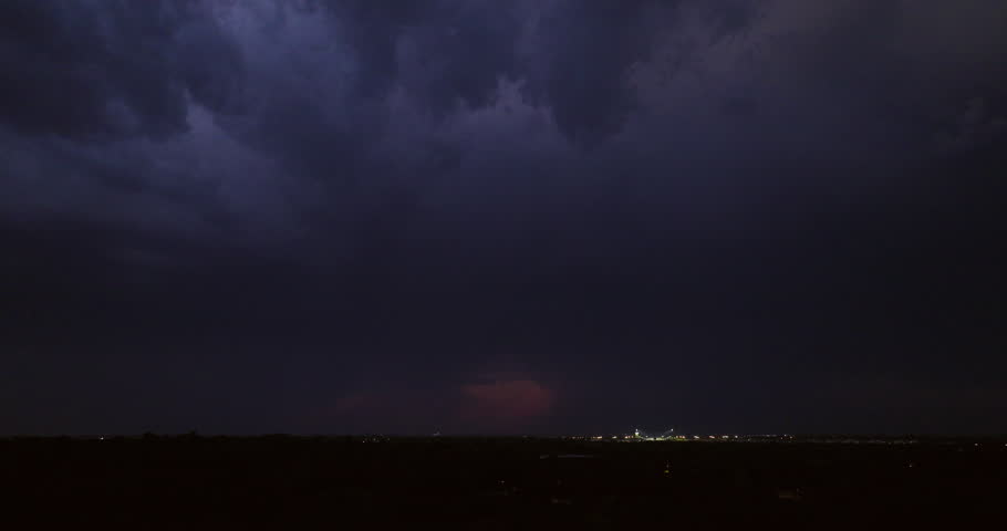 Cinematic aerial of dark storm clouds with dramatic lightning bolts striking brightly after dusk in a dark sky with an ominous tone in this suburban establishing shot showing the power of nature.