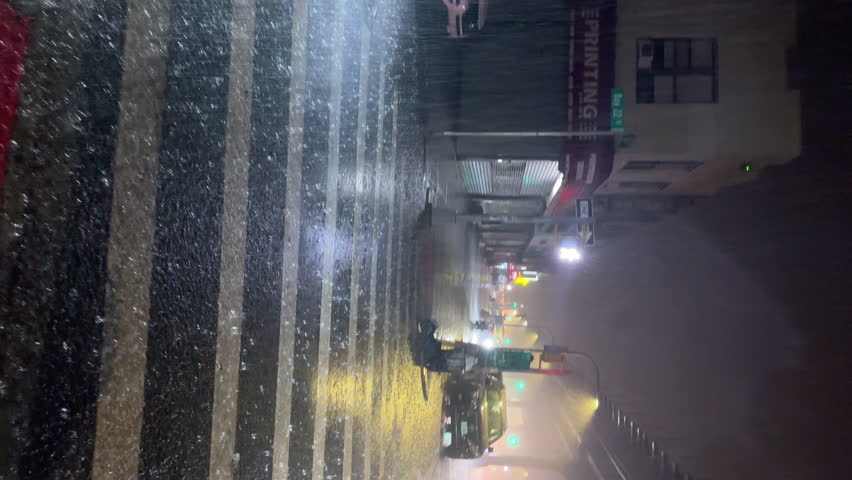 NYC, USA - SEPTEMBER 9, 2023: POV vertical view, walking along the night street under extremely heavy rain in Brooklyn. View of the parked cars, closed stores, street lights. Autumn stormy weather
