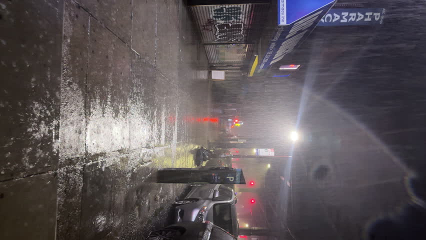 NYC, USA - SEPTEMBER 9, 2023: POV vertical view, walking along the night street under heavy rain in Brooklyn. View of the parked cars, pharmacy, street lights and houses. Autumn stormy weather