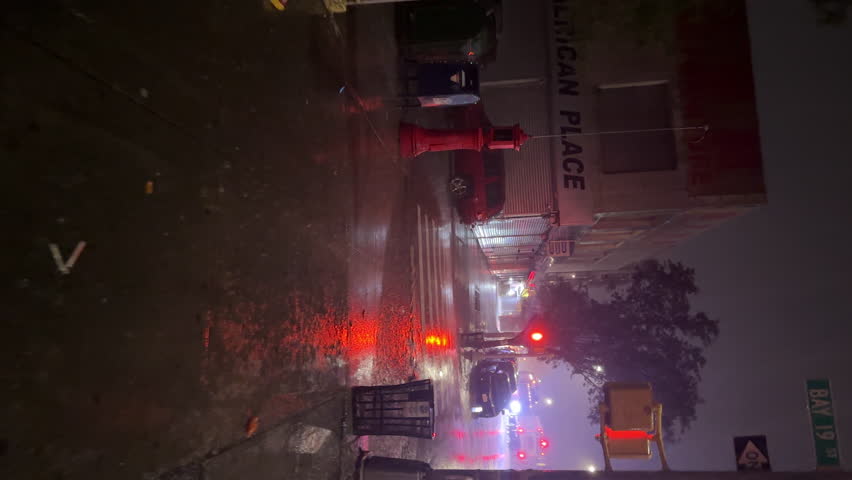 NYC, USA - SEPTEMBER 9, 2023: POV vertical view, walking along the night street under extremely heavy rain in Brooklyn. View of closed stores, street lights. Autumn stormy weather