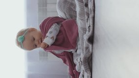 Vertical video. Cute baby girl playing with diaper while sitting on the floor in messy nursery room