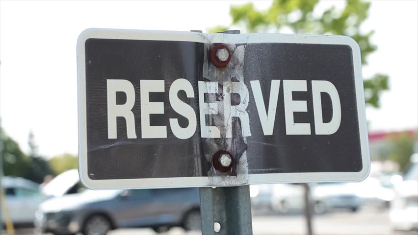 reserved horizontal rectangle black white sign on metal post with parking lot cars behind