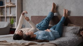 Caucasian happy couple lying upside down together on comfort bed relax with mobile phone scrolling social network buying online internet shopping relaxed woman wife and man husband leisure in bedroom - Powered by Shutterstock - Get 15% off with code: PIKWIZARD15