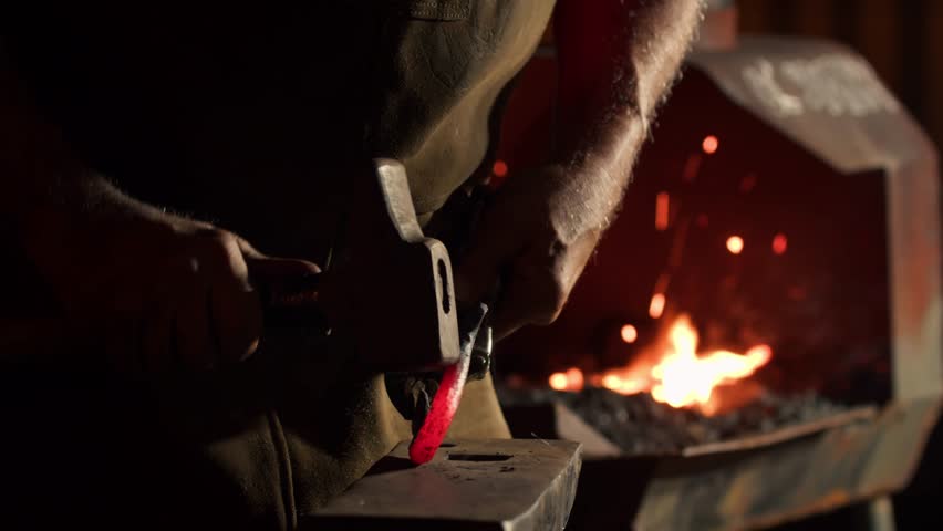 Authentic Blacksmith Man Forges a Metal Product in Dark Outside. Close-up of a Blacksmith in an Apron Working with a Hammer and Iron in an Outdoor Workshop.  Royalty-Free Stock Footage #1109147327
