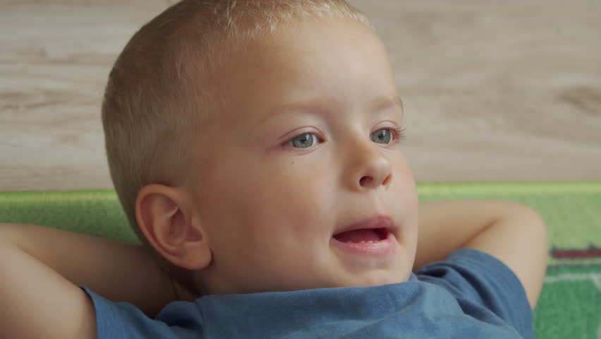 child is lying on the floor with his hands behind his head, little boy watching TV