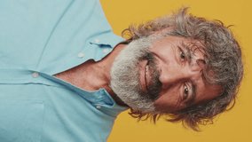 Vertical video, Close-up of an elderly grey-haired bearded man wearing a blue shirt, looking at the camera and laughing isolated on an orange background in the studio - Powered by Shutterstock - Get 15% off with code: PIKWIZARD15