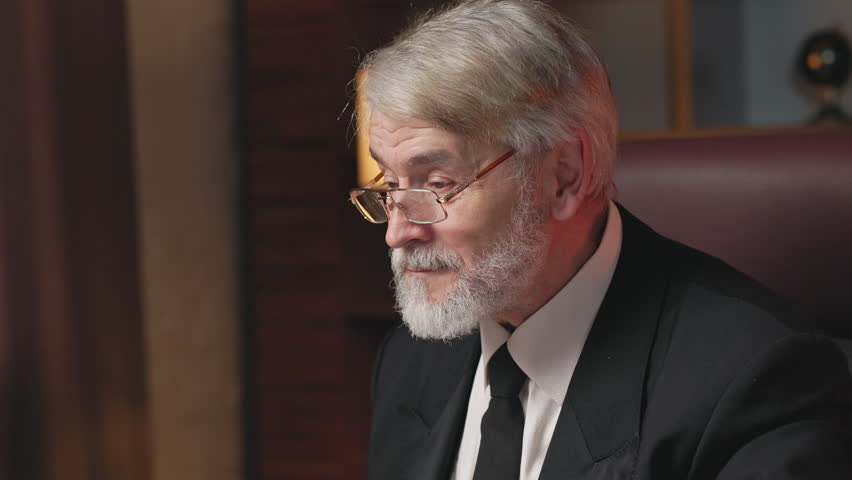 Close up view of confident grey-haired man taking off glasses while being deep in his thought during office hours. Focused older entrepreneur in formal clothes viewing presentation from employees.