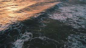 A sea wave with a sunset glow rolls onto the shore. Tropical beach, top view. An aerial view of the sea coast. Panorama view of the evening beach. Aerial video of sea waves. Ocean and beach.