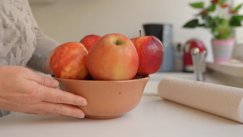 Woman puts ripe washed large red apples in ceramic bowl, in home kitchen, preparing for cooking | Shutterstock HD Video #1109166041