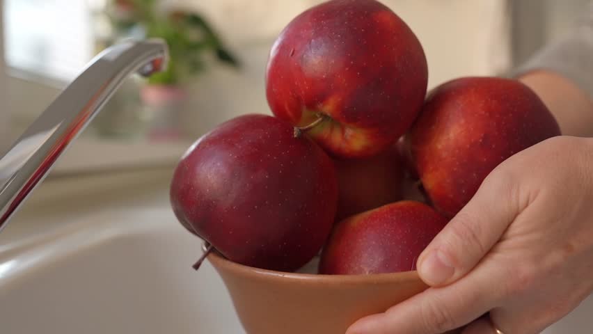 Woman puts ripe washed large red apples in ceramic bowl, in home kitchen, preparing for cooking | Shutterstock HD Video #1109166043